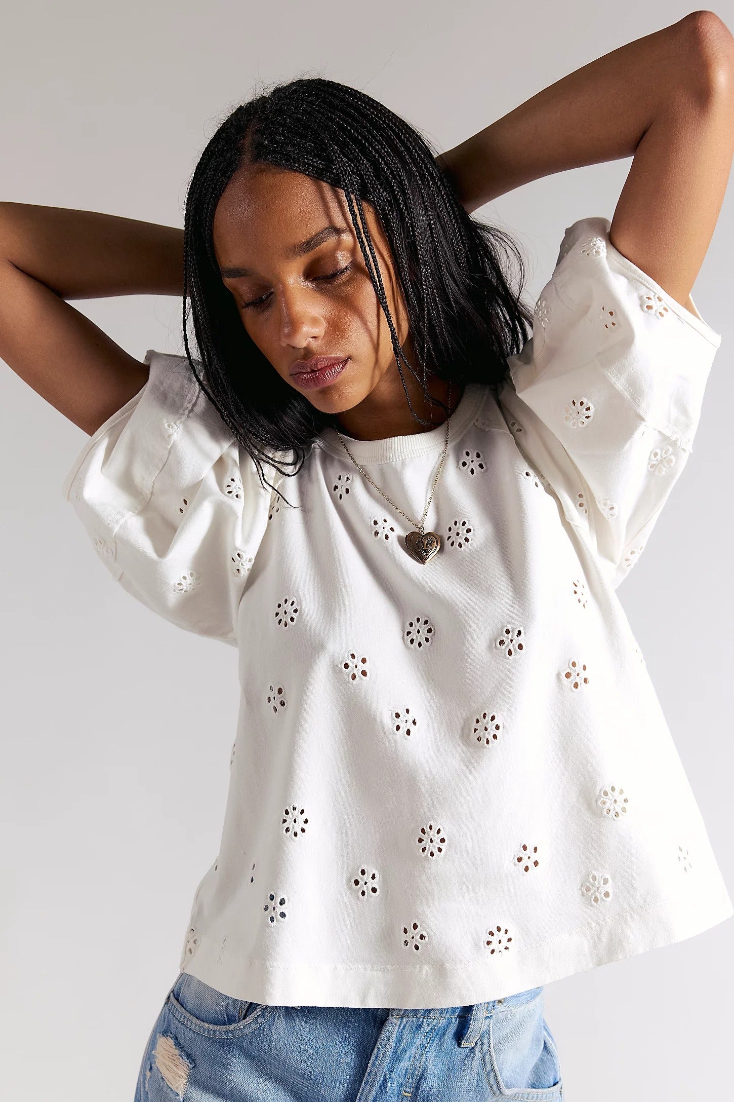 Woman wearing a white blouse with floral cut-out details on a plain background