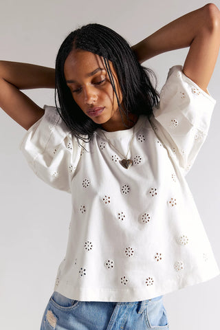 Woman wearing a white blouse with floral cut-out details on a plain background