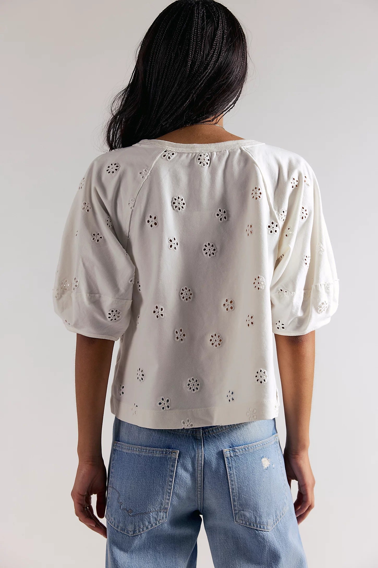 Person wearing a light-colored blouse with floral patterns and blue jeans against a plain background