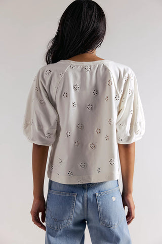 Person wearing a light-colored blouse with floral patterns and blue jeans against a plain background