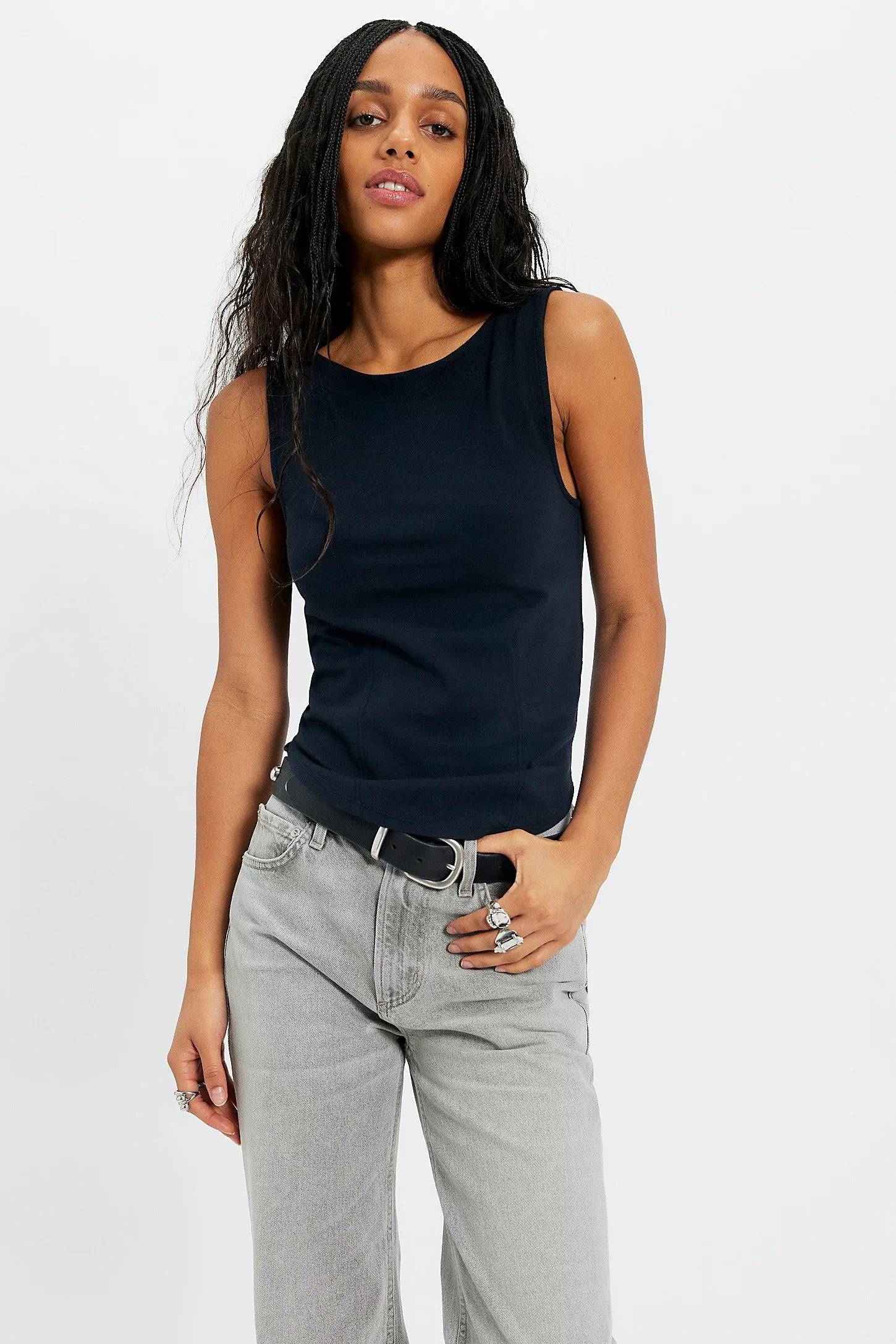 Woman wearing a black sleeveless top and gray jeans on a white background