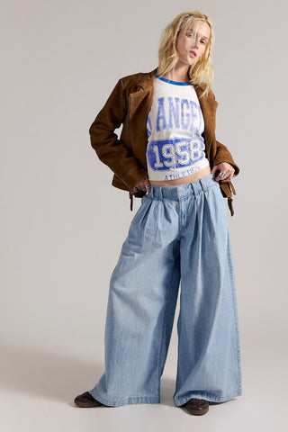 Person wearing a brown jacket, white t-shirt with text, and blue jeans on a plain background