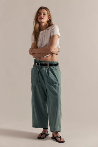 Woman wearing a white t-shirt and green pants against a beige background