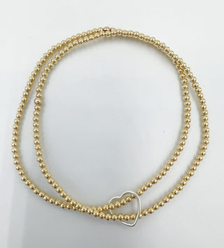 a double layer gold beaded bracelet with a silver heart charm