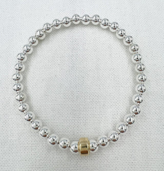 Silver beaded bracelet with a gold accent on a light fabric background
