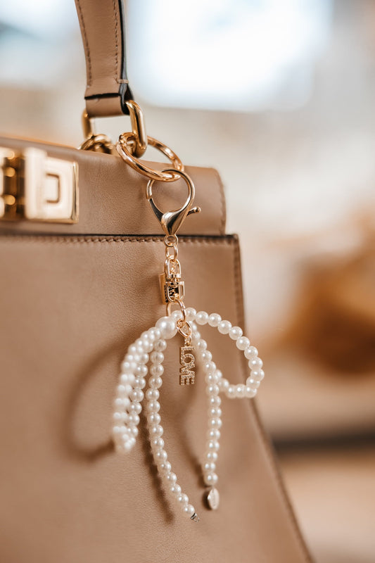 Pearl keychain with gold clasp attached to a beige handbag.