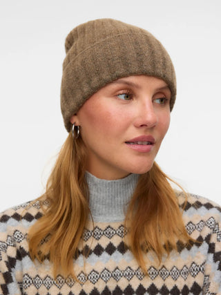 Woman wearing a brown knit beanie and patterned sweater against a light background