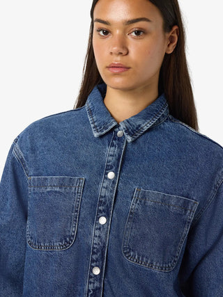 Person wearing a blue denim shirt against a plain background