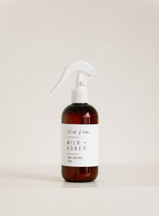 A brown glass spray bottle labeled 'Milk + Honey Room + Linen Spray' on a white background.