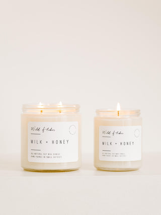 Two candles with white labels reading 'Milk + Honey', one in a smaller jar and one in a larger jar, both on a white background.