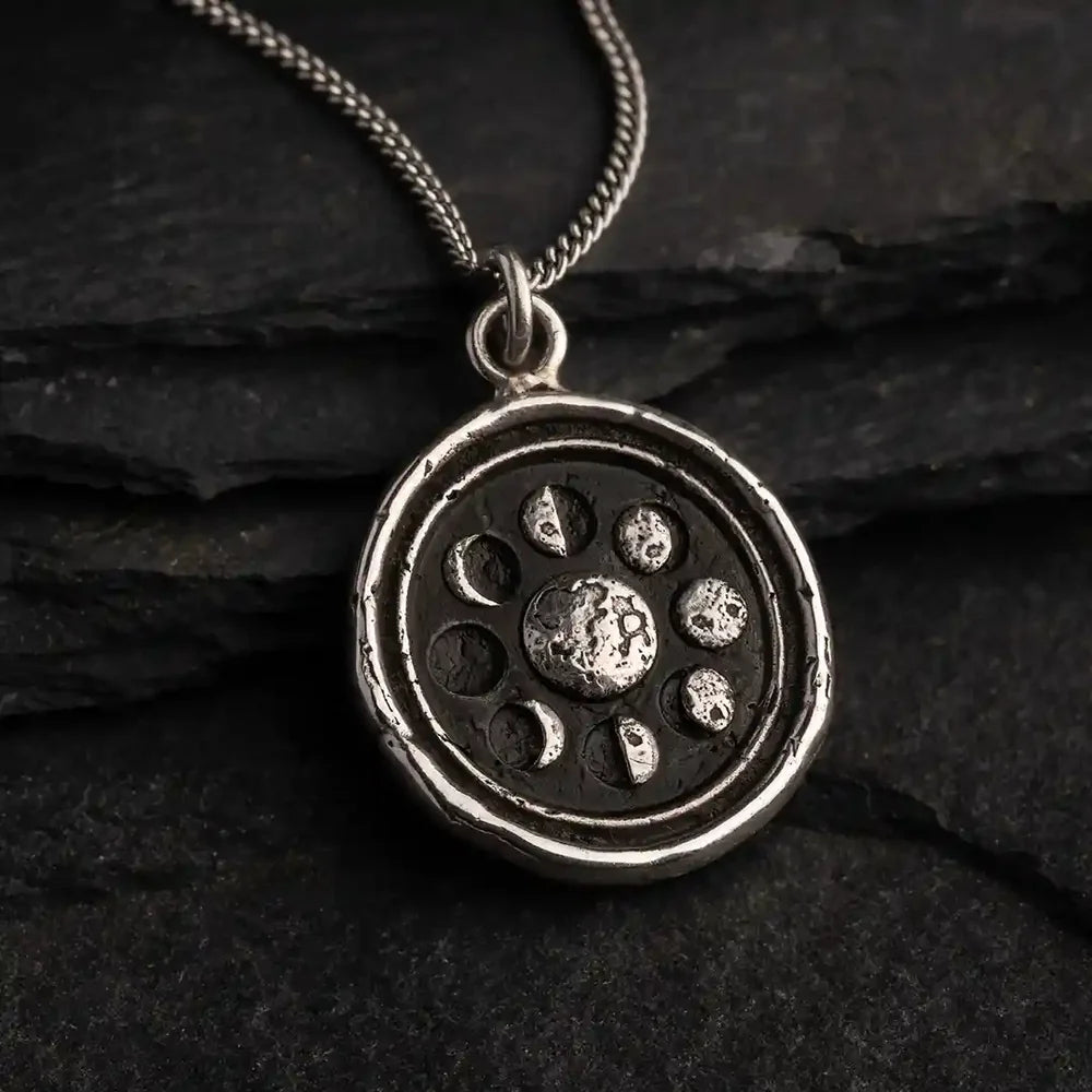 Silver pendant with celestial design on a dark stone surface