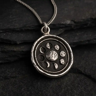 Silver pendant with celestial design on a dark stone surface