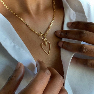 a person wearing a gold chainlink necklace with a heart pendant 