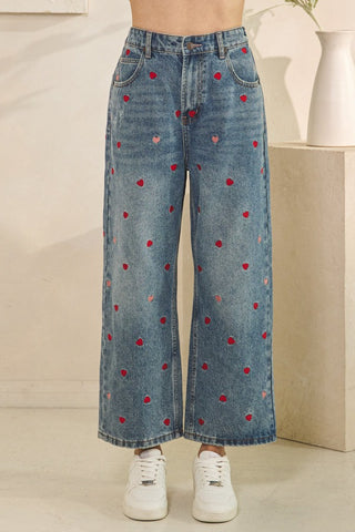 Blue jeans with red heart patterns worn by a person indoors.