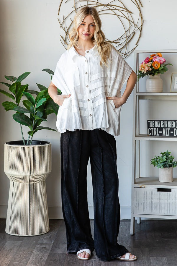 Woman in a white blouse and black pants standing in a room with plants and decor.