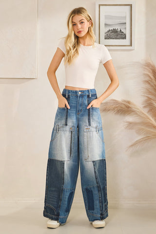 Woman wearing a white top and blue patchwork jeans standing in a room with a framed picture on the wall.