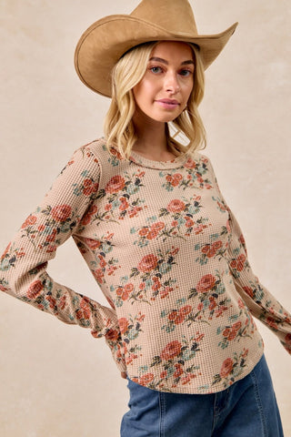 Woman wearing a floral long-sleeve top and cowboy hat against a beige background