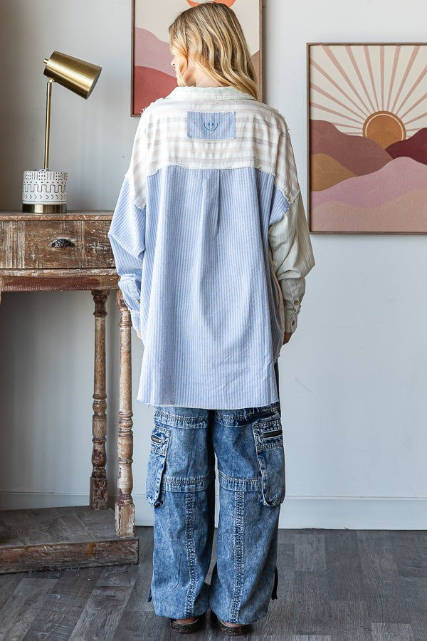 Person wearing a light blue and beige striped shirt with a white collar in a room with a wooden table and wall art.