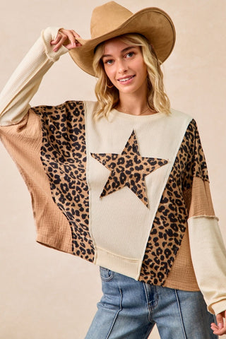 Woman wearing a sweater with a star design and leopard print pattern, holding a cowboy hat.