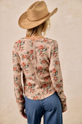 Person wearing a floral blouse and cowboy hat against a beige background