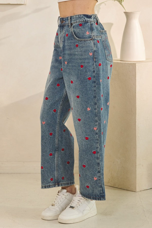 Blue jeans with heart patterns worn by a person on a neutral background