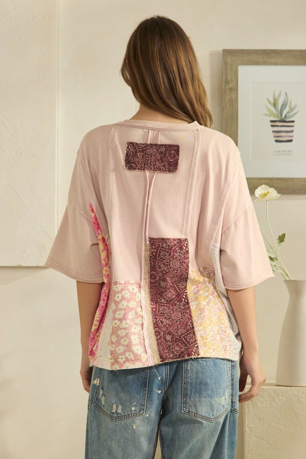 Person wearing a patchwork shirt with floral and paisley patterns, standing in a room.