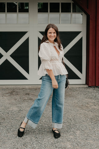 Woman in a white blouse and blue jeans standing in front of a barn door.