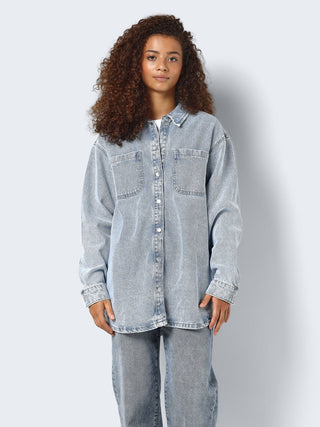 Person wearing a light blue denim shirt and jeans on a plain background
