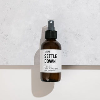 Brown spray bottle labeled 'Settle Down' on a light gray background