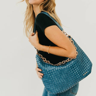 Women wearing a blue woven shoulder bag against a neutral photo background. 