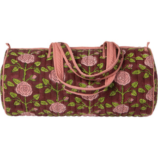 A quilted duffel bag with a floral pattern featuring pink roses and green leaves on a dark reddish-brown background, with pink handles, shown against a plain white background.