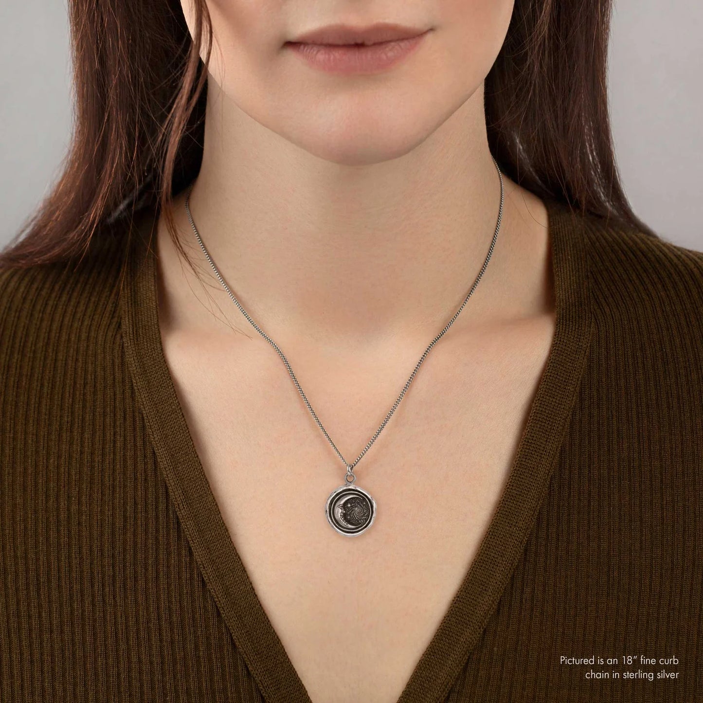 Woman wearing a silver necklace with a pendant against a neutral background