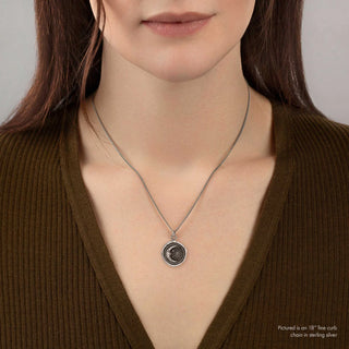 Woman wearing a silver necklace with a pendant against a neutral background