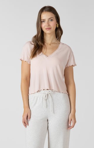 Woman wearing a light pink top and white pants on a plain background