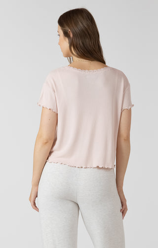 Woman wearing a light pink top and white pants on a plain background