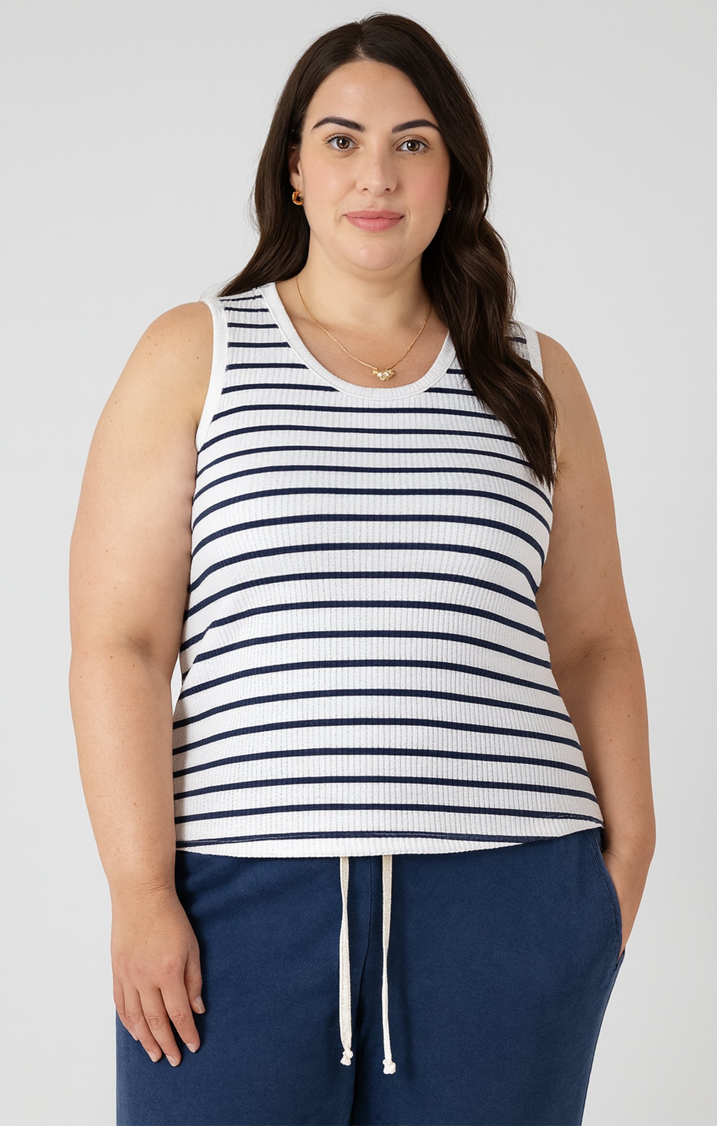 Woman wearing a striped tank top and navy pants against a white background