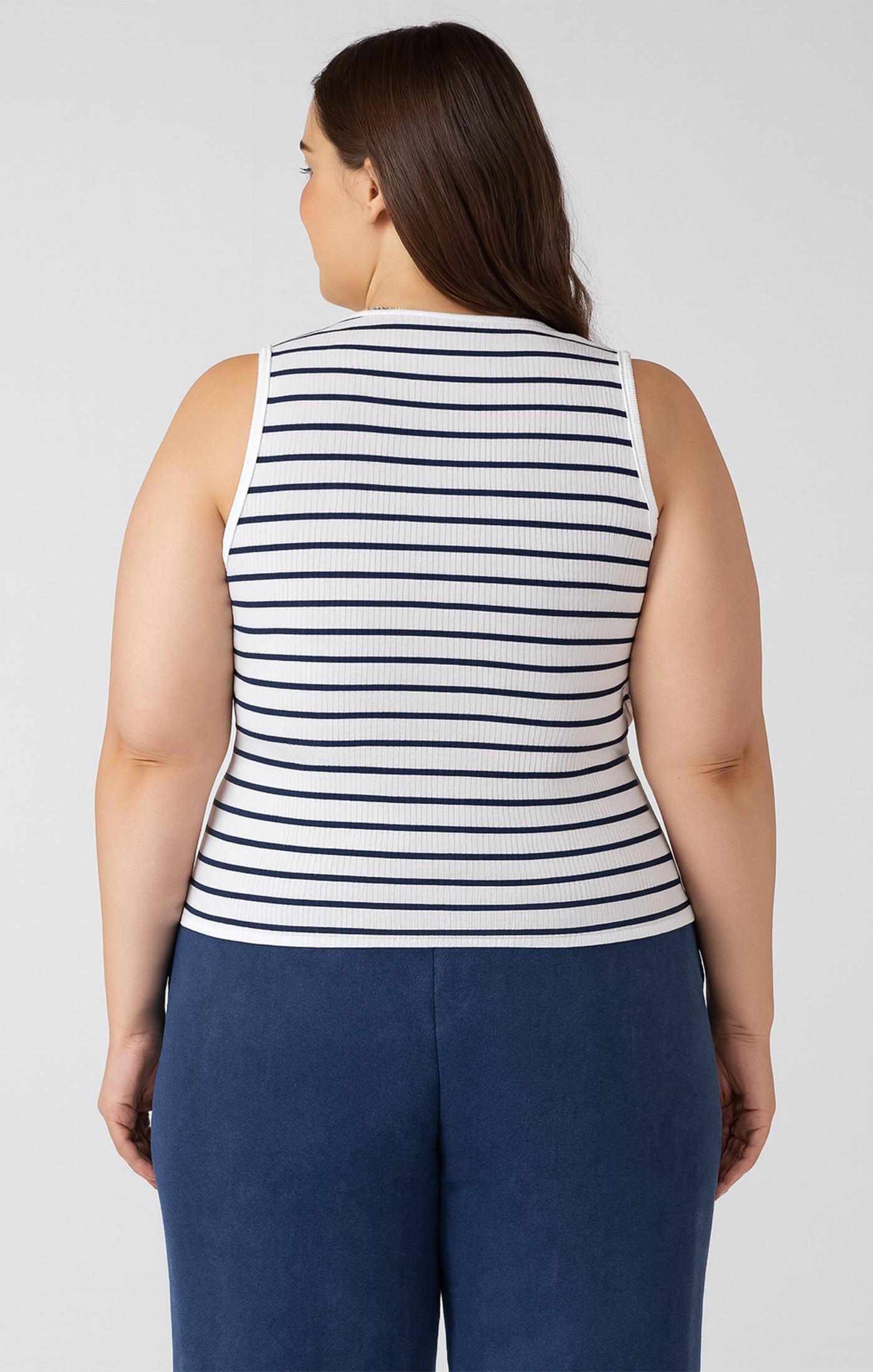 Woman wearing a striped sleeveless top and navy pants on a plain background