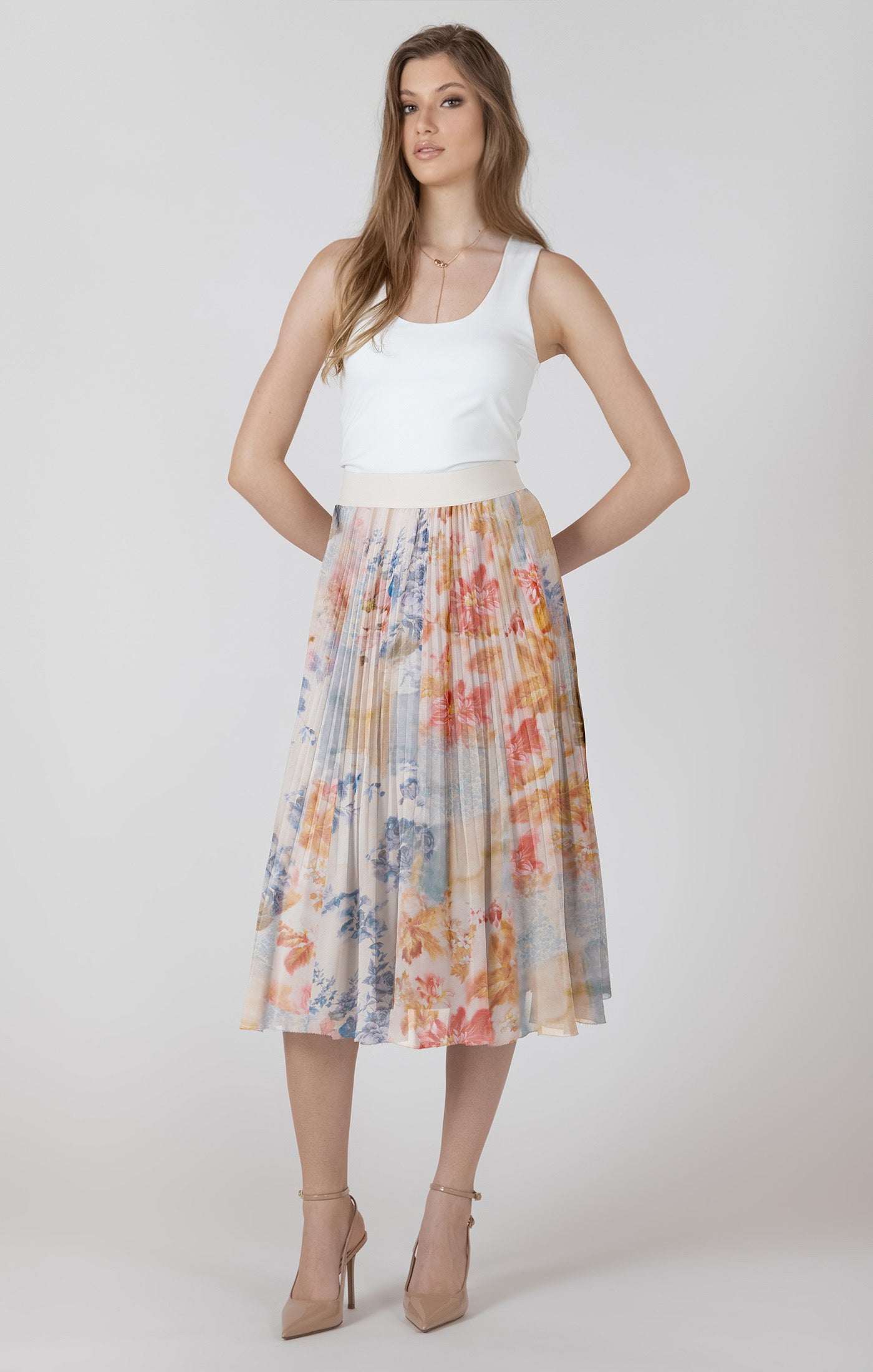 Woman wearing a white top and colorful pleated skirt on a plain background