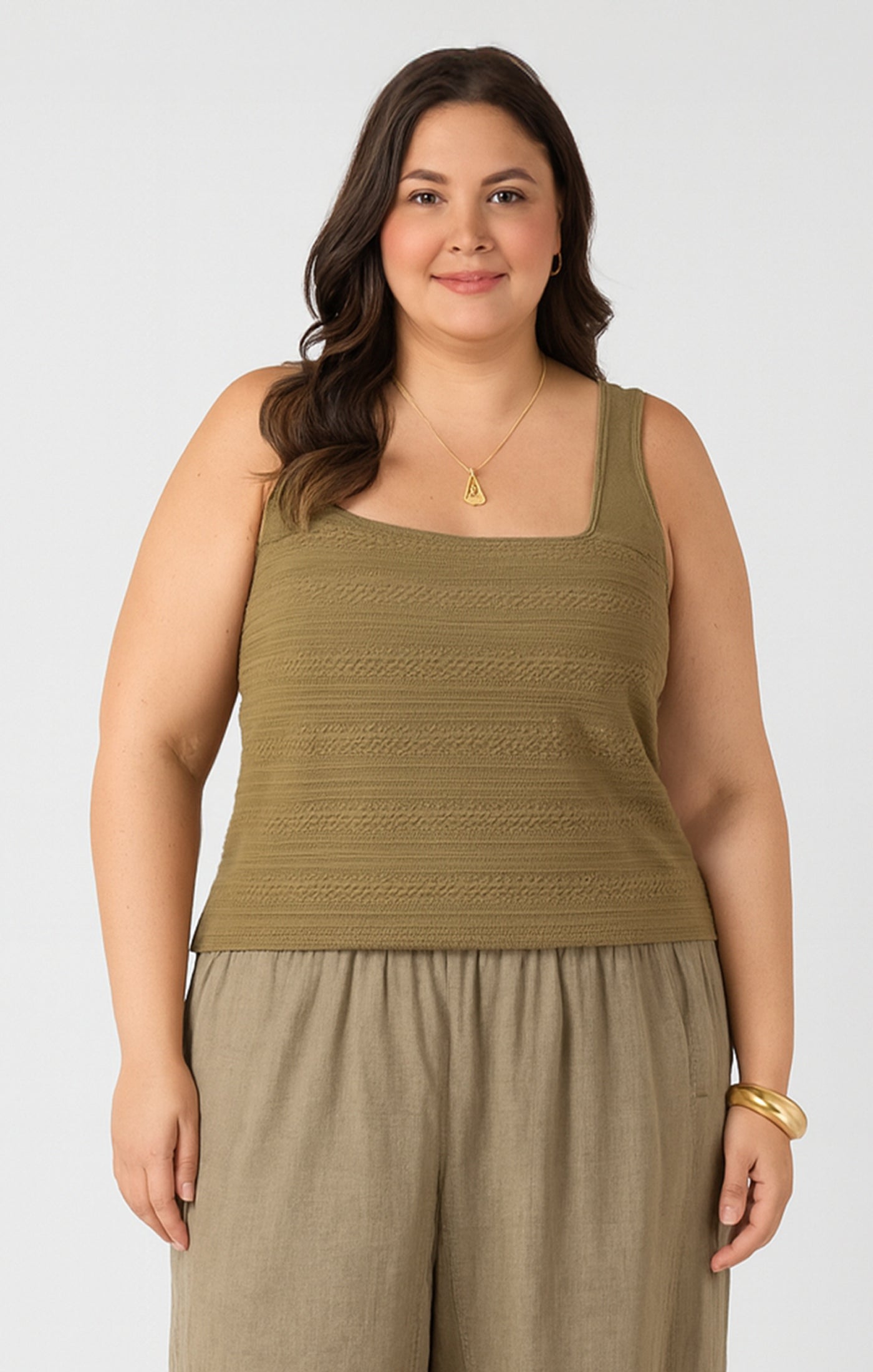 Woman wearing a green sleeveless top and beige pants on a white background