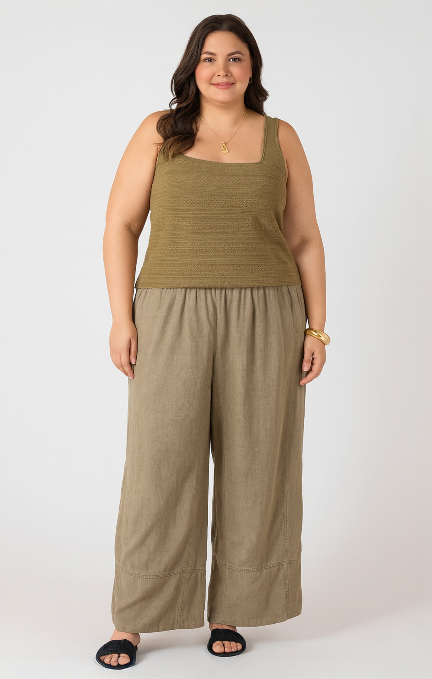 Woman wearing a green tank top and beige wide-leg pants on a white background