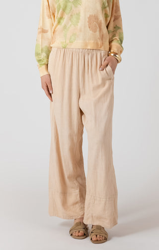 Person wearing a tie-dye shirt and beige wide-leg pants on a white background