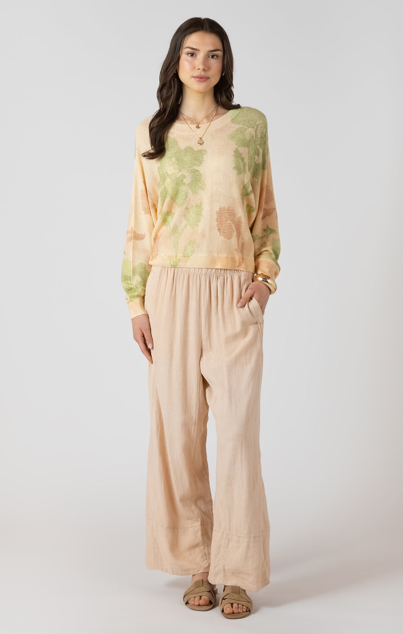 Woman wearing a green and beige patterned top with beige pants on a white background