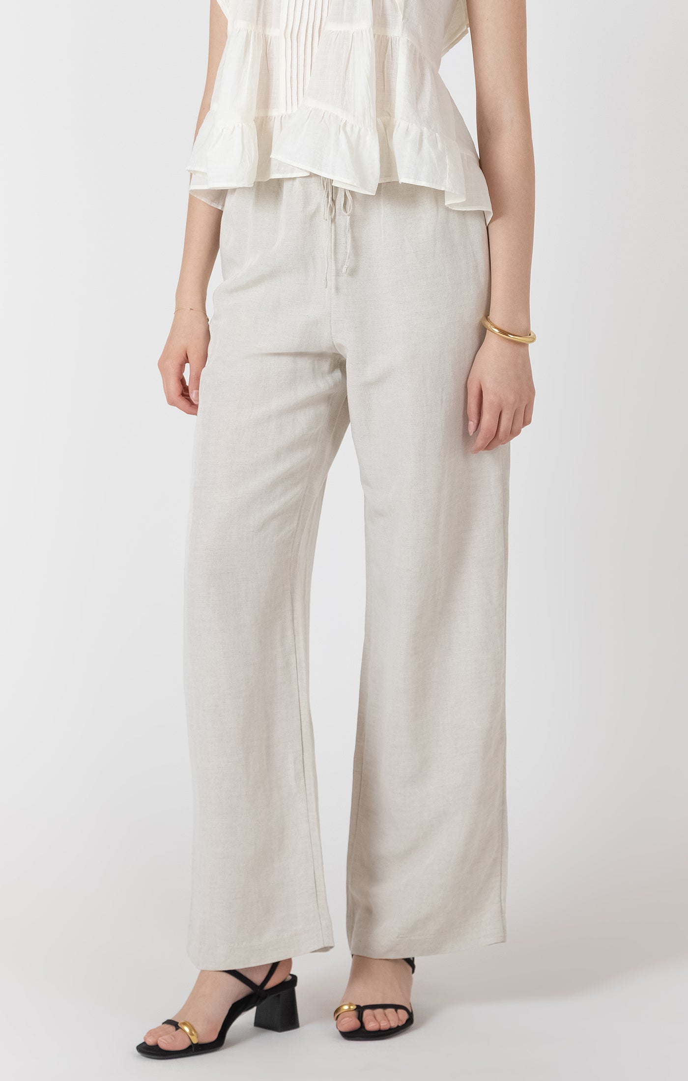 Person wearing light-colored pants and a white top on a plain background