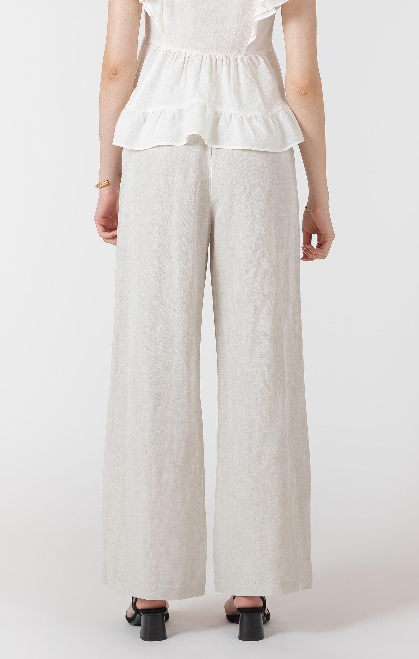Person wearing a white ruffled top and beige wide-leg pants on a white background