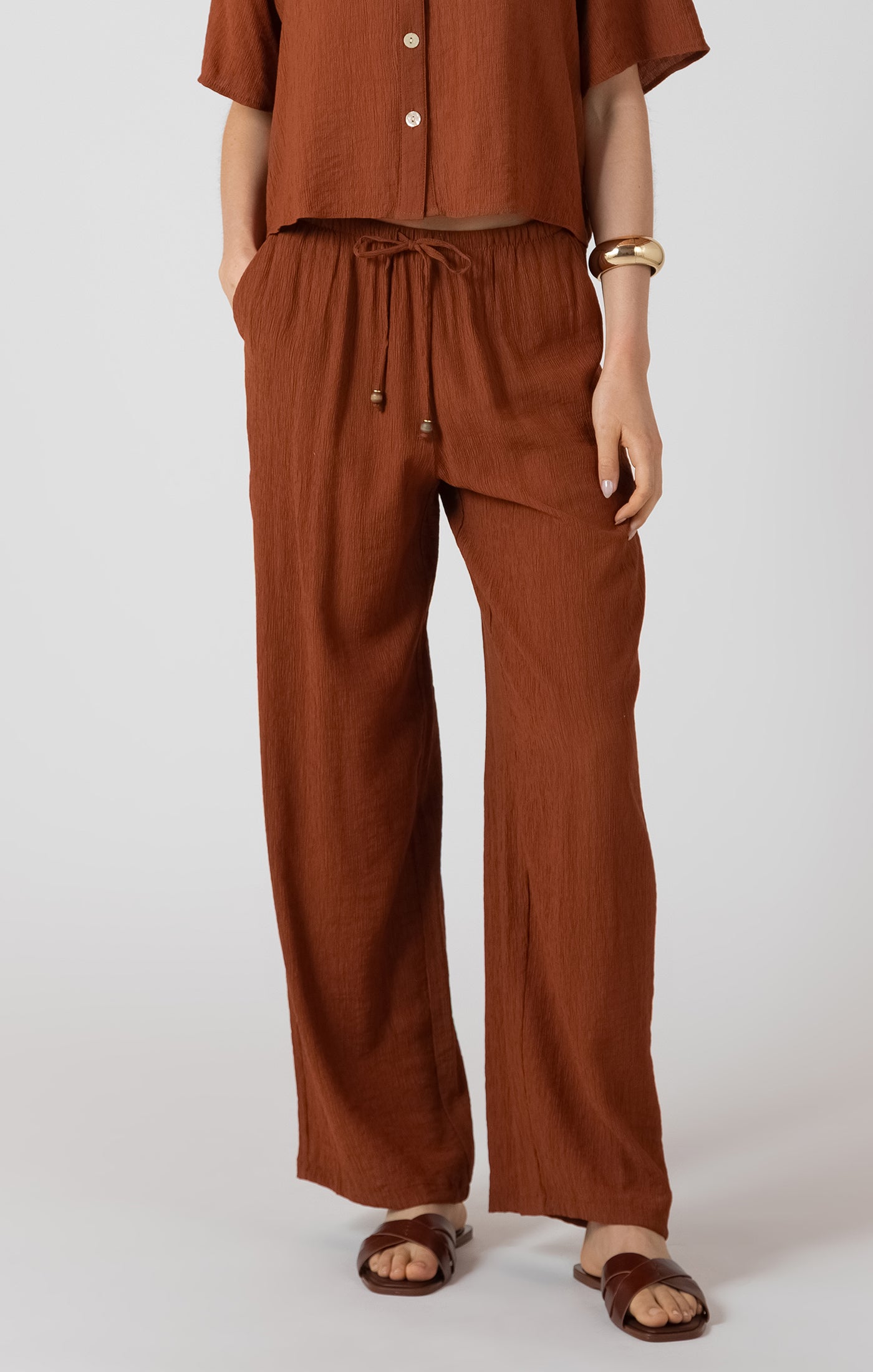 Person wearing a brown outfit with wide-leg pants and a cropped top on a white background