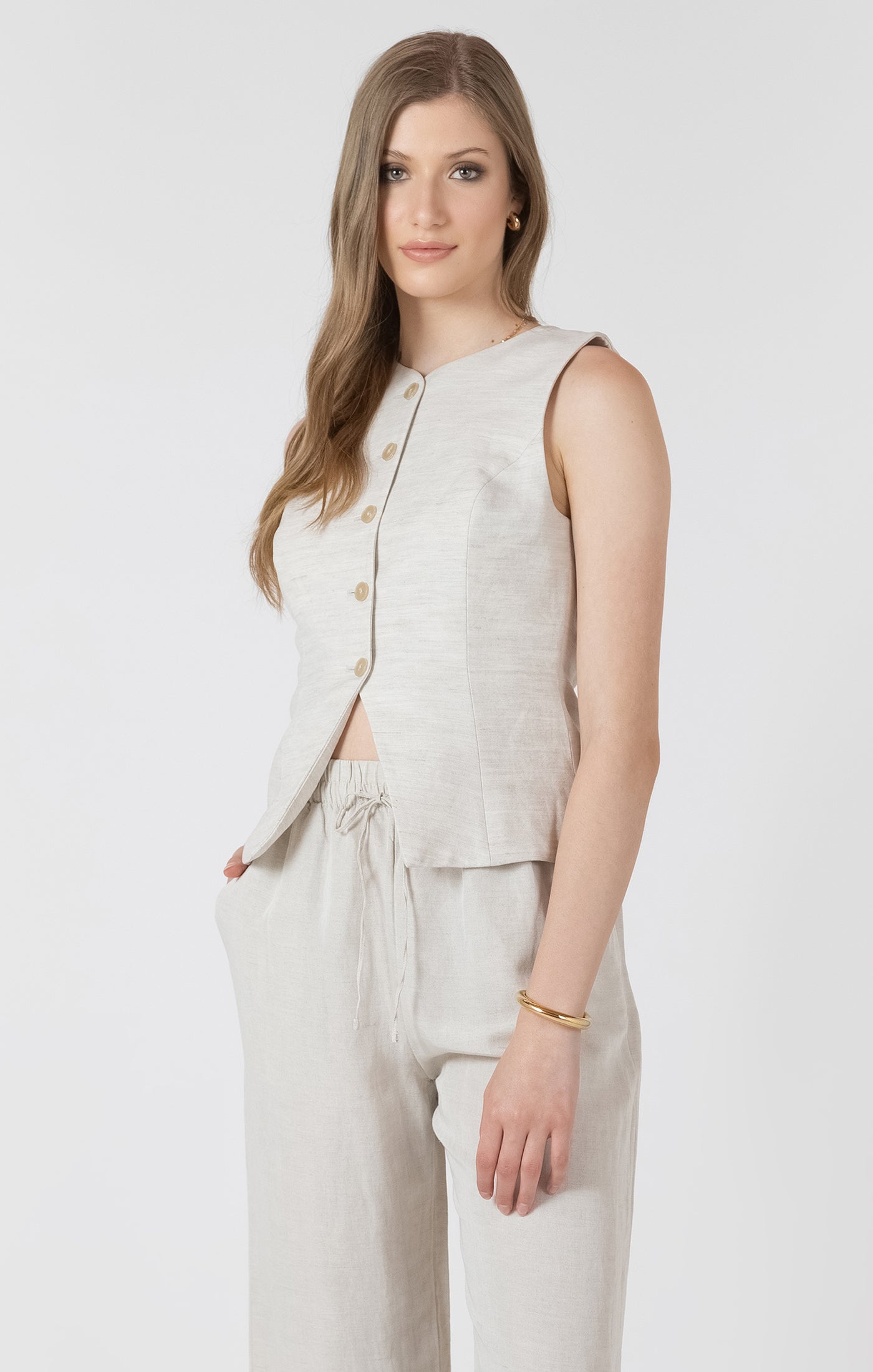 Woman wearing a beige sleeveless top and pants on a white background