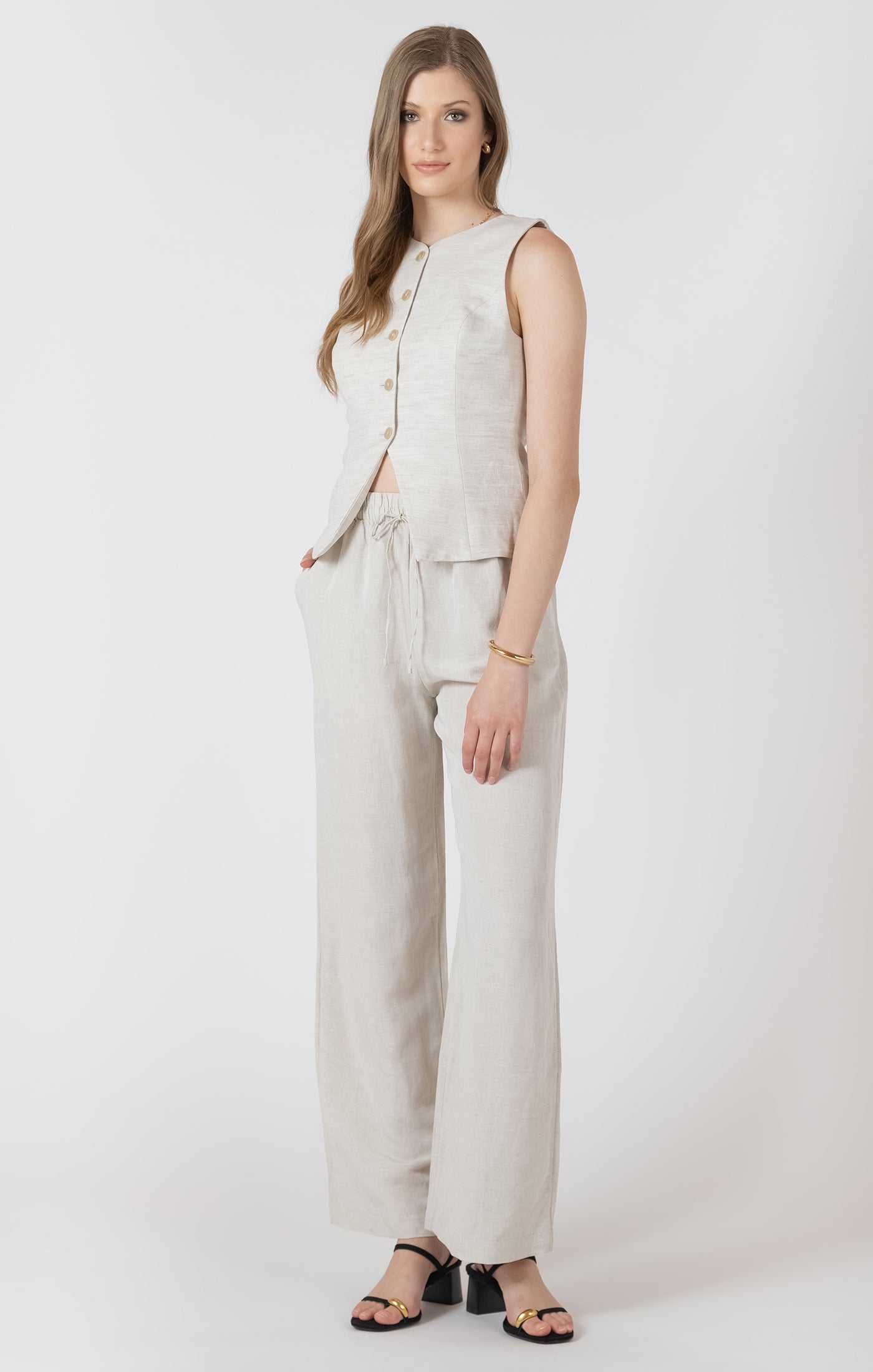 Woman wearing a beige sleeveless top and pants on a white background