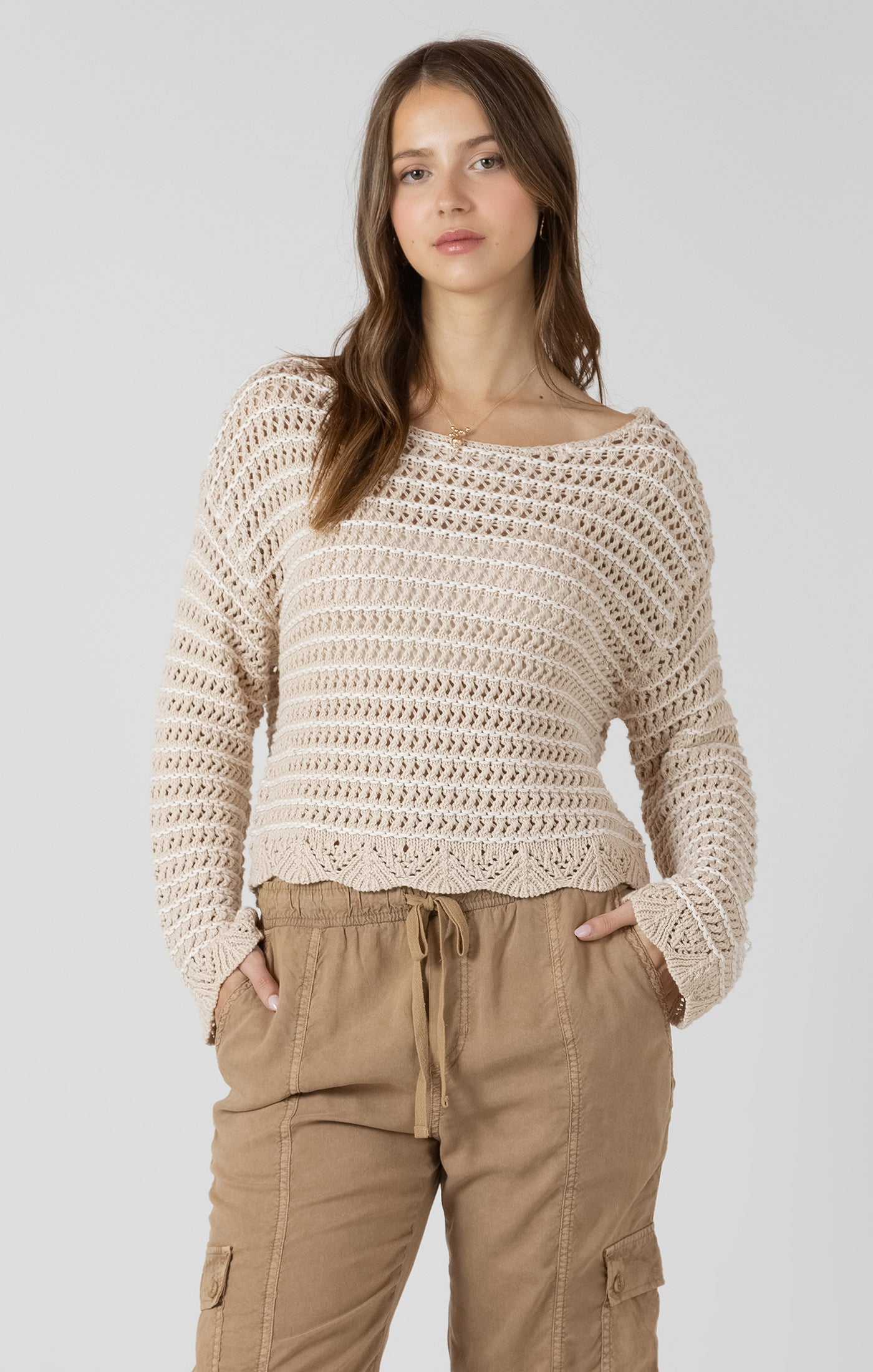 Woman wearing a beige crochet sweater and brown pants on a white background