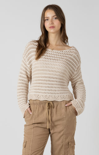 Woman wearing a beige crochet sweater and brown pants on a white background