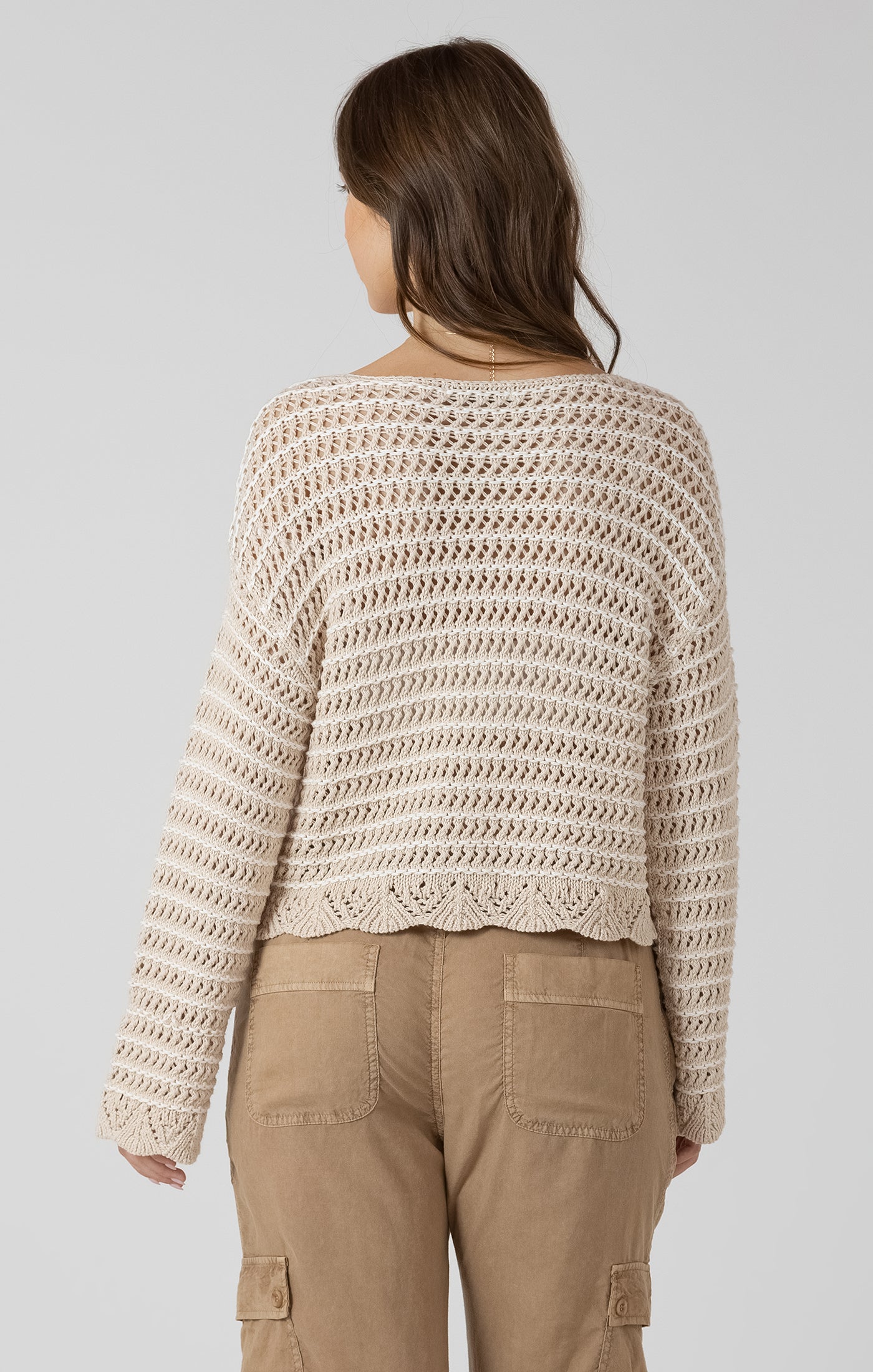 Woman wearing a beige crochet sweater and brown pants on a plain background